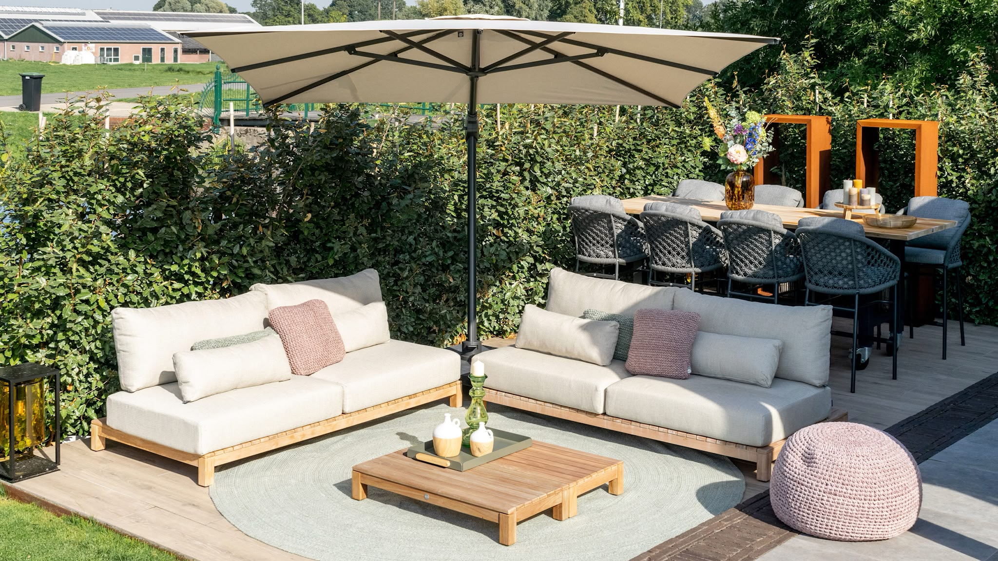 Loungetuin met teak buitenmeubelen, parasol en strakke beukenhaag